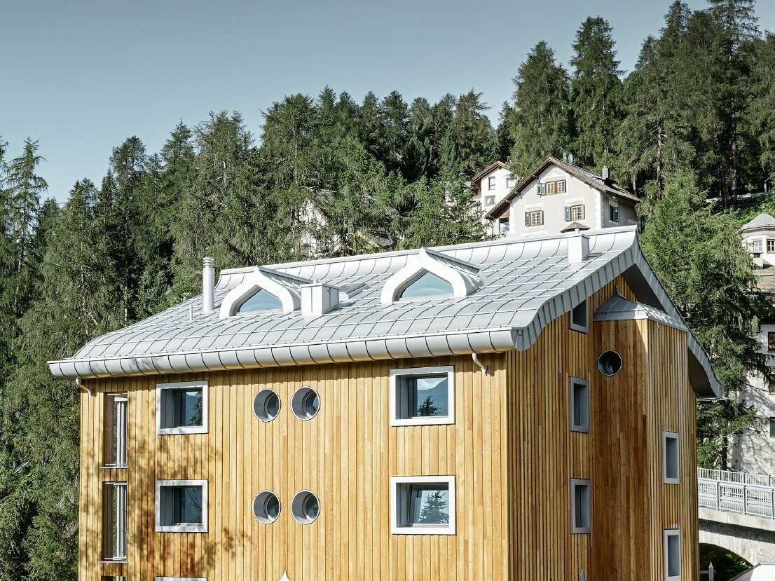 Complesso residenziale a St. Moritz con facciata in legno e copertura in alluminio con grondaia curva in silver metallizzato