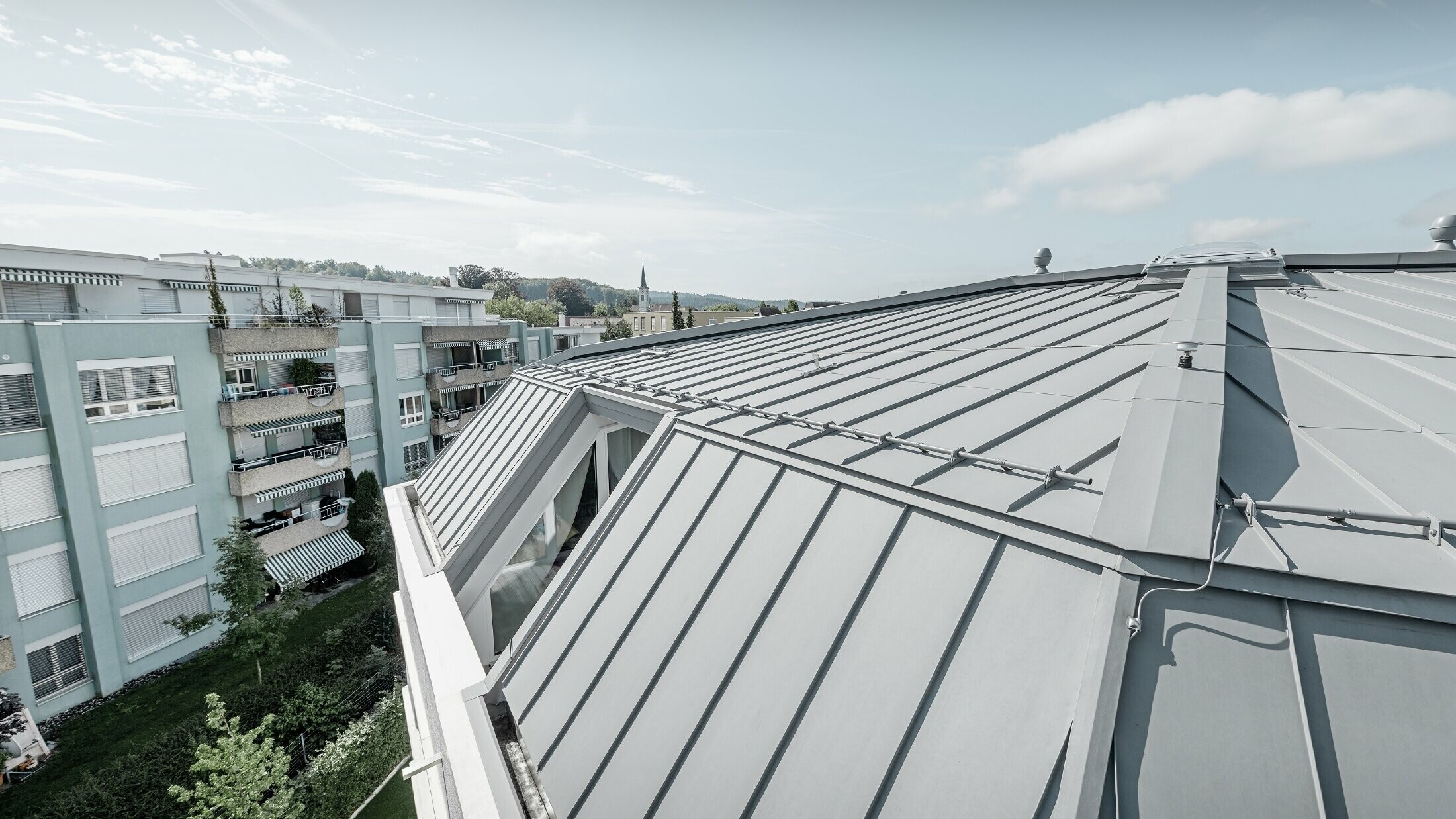 Immagine dettagliata della superficie del tetto di un condominio; tetto con aggraffatura realizzato con Prefalz PREFA in grigio patina.