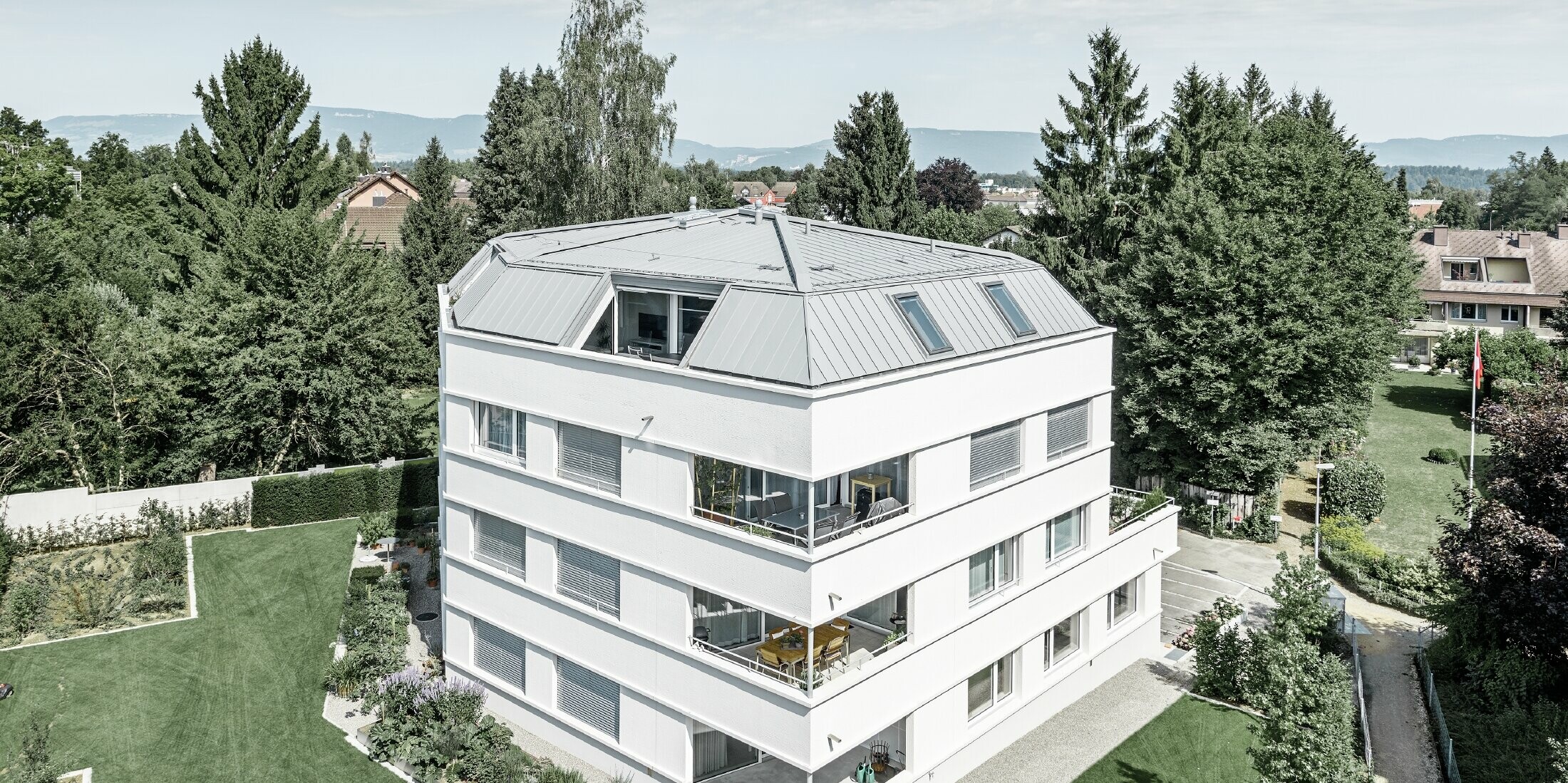 Schlichtes Mehrfamilienhaus mit PREFA Prefalz in Patina Grau; Die Fassade ist weiß verputzt mit großzügigen Loggien an der Außenecke.