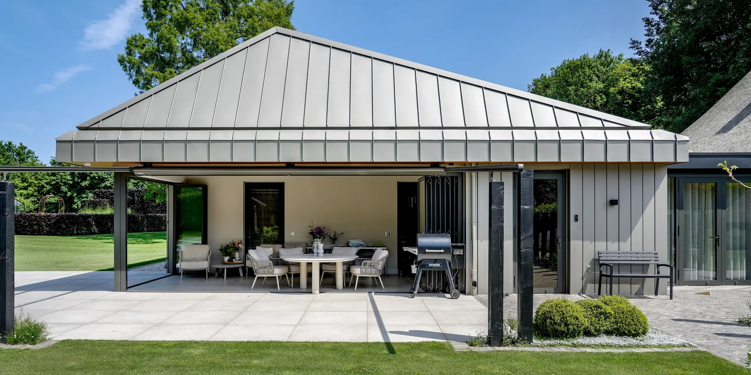 Frontalansicht des modernen Erweiterungsbaus in Putten mit durchgängiger PREFALZ Aluminiumverkleidung für Dach und Fassade. Die präzisen Stehfalze, die klar definierte Dachform und die großzügigen Glasflächen schaffen eine elegante, zeitlose Architektur. PREFA Aluminium überzeugt durch langlebige Qualität, hohe Witterungsbeständigkeit und eine harmonische Einbindung in die weitläufige Gartenlandschaft.