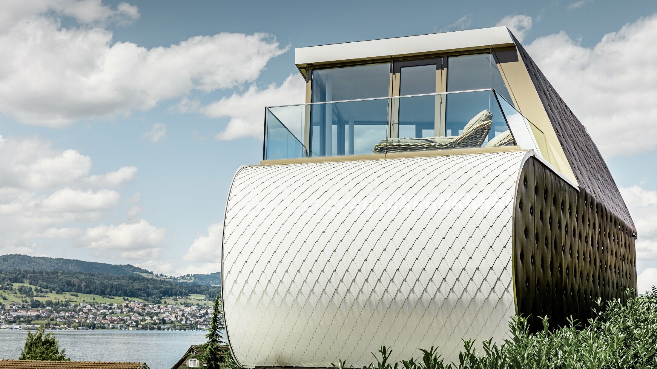 Seitliche Ansicht des ausgezeichneten Flexhouse, entworfen durch Architekt Camenzind; Man sieht eine der geschwungenen Außenwände, die mit der schuppigen Alu-Fassade von PREFA in Reinweiß verkleidet ist.