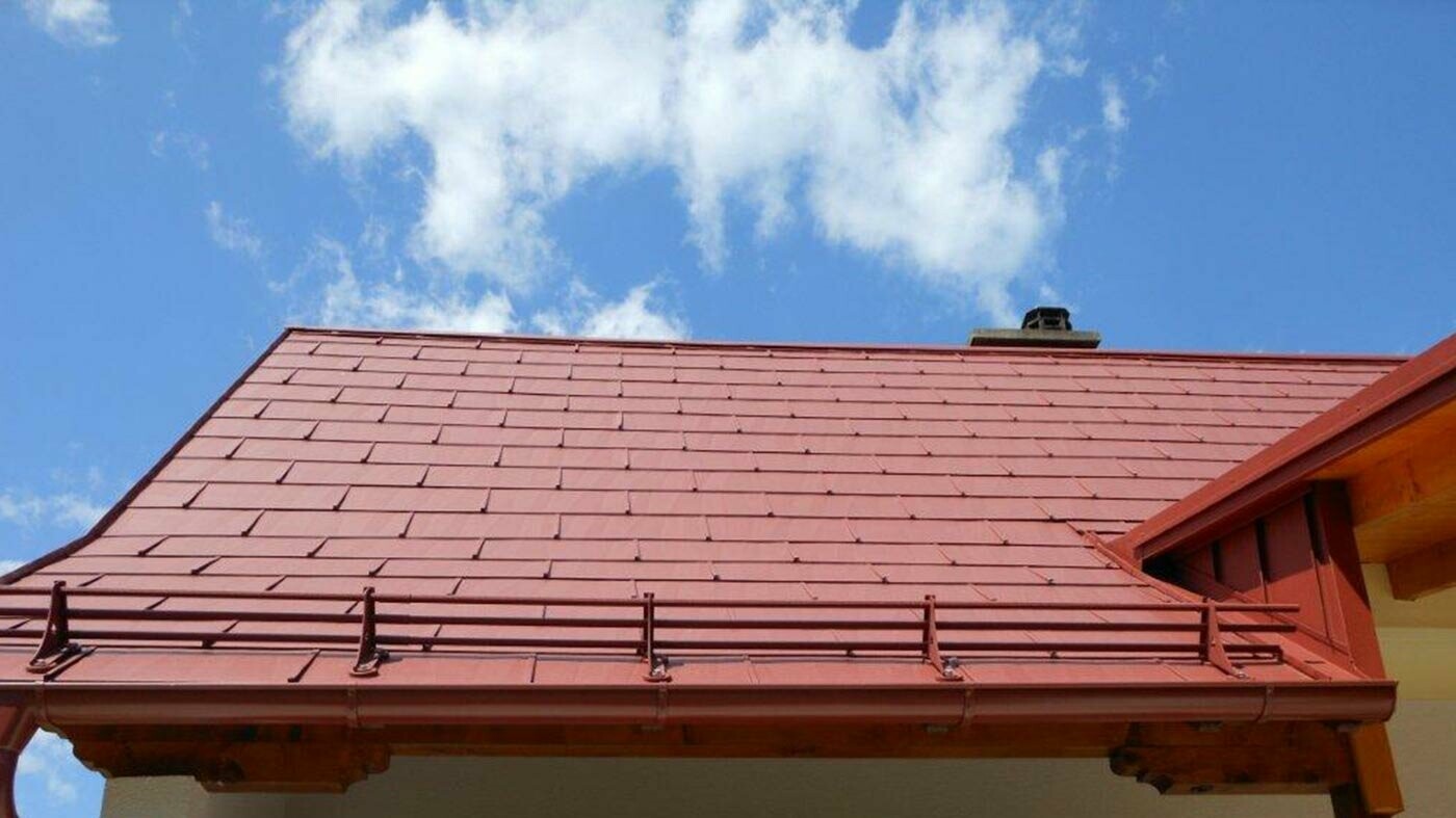 Immagine dettagliata di una superficie di tetto con pannello FX.12 PREFA di colore marrone rame, con sistema di raccolta della neve.