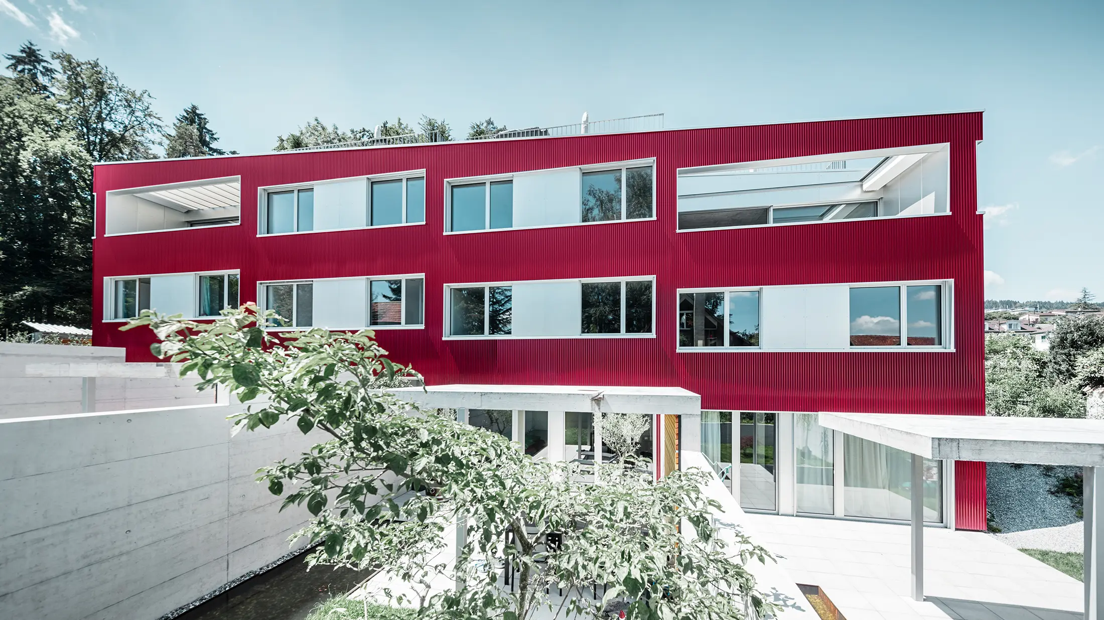 Complesso residenziale con tetto piano e balconi con facciata rosso vino con profilo ondulato PREFA 