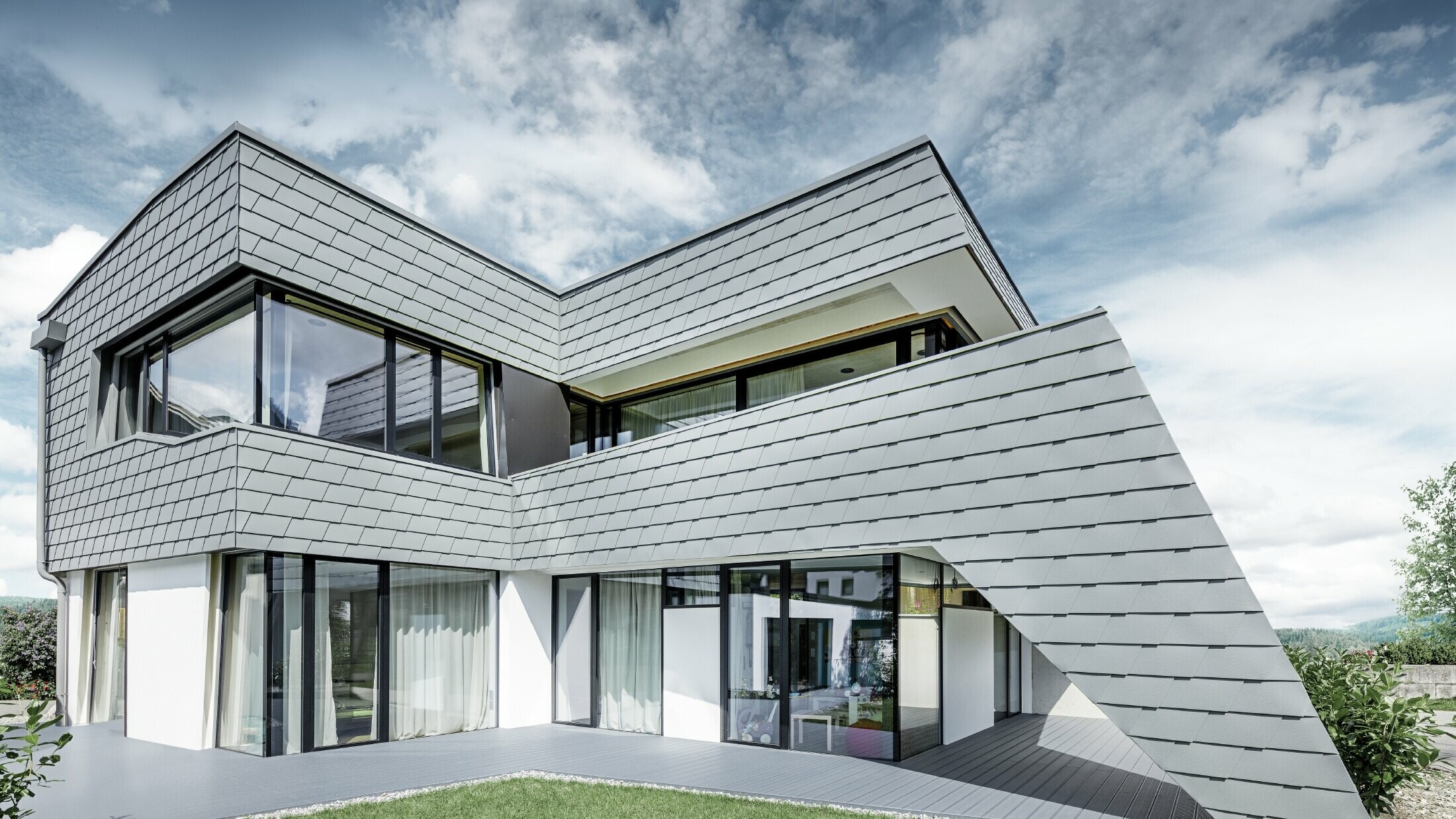 Casa unifamiliare moderna con copertura piana, ampie superfici vetrate e una facciata in scandola in grigio chiaro in alluminio PREFA