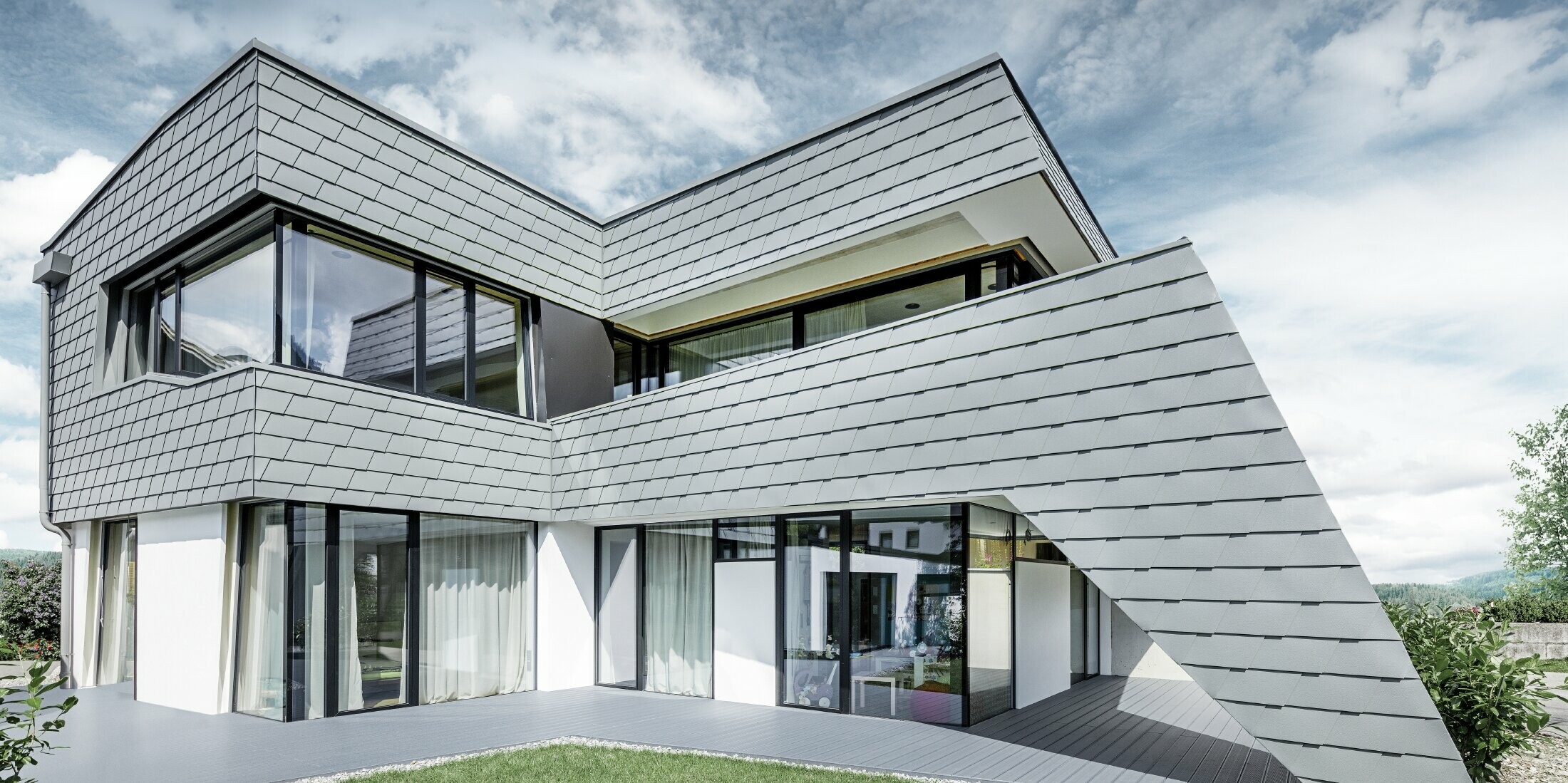 Modernes Einfamilienhaus mit Flachdach, großen Fensterflächen und einer Schindel-Fassade in hellgrau aus Aluminium von PREFA