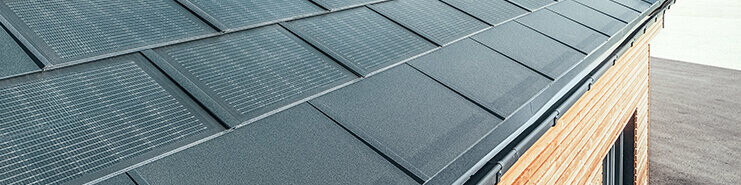 Tegola fotovoltaica PREFA in formato grande abbinata alla tegola R.16 in nero, canale quadro e facciata in legno di larice