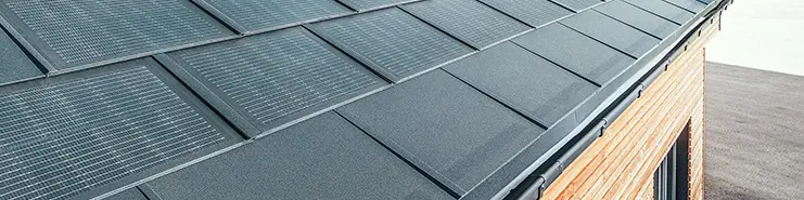 Tegola fotovoltaica PREFA in formato grande abbinata alla tegola R.16 in nero, canale quadro e facciata in legno di larice