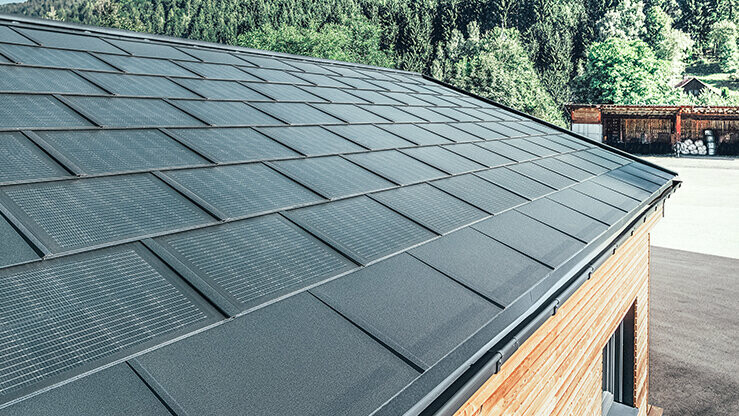 Tegola fotovoltaica PREFA in formato grande abbinata alla tegola R.16 in nero, canale quadro e facciata in legno di larice
