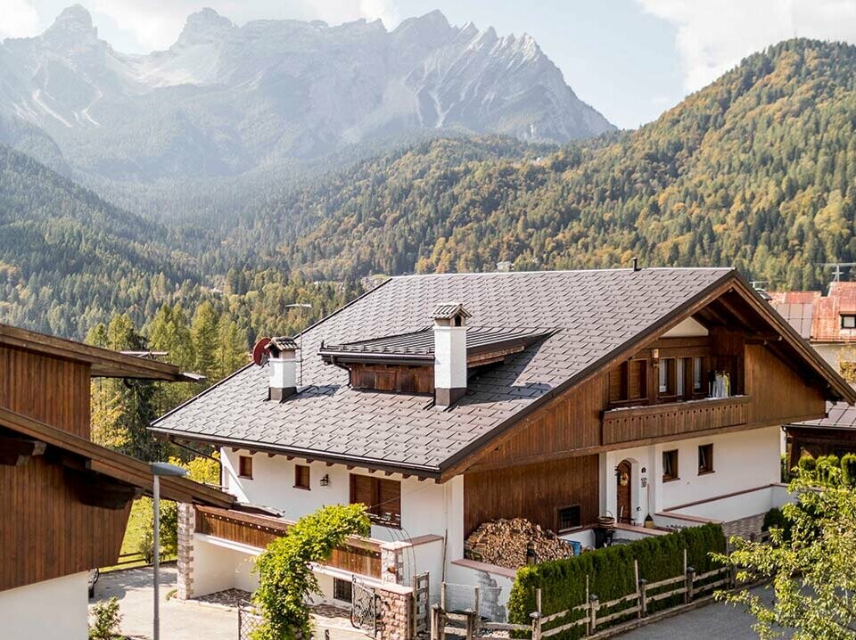 Dieses Wohnhaus in den Dolomiten wurde mit PREFA Dachplatten R.16 in P.10 Nussbraun eingedeckt, das traditionelle Haus liegt inmitten der Berge in Italien