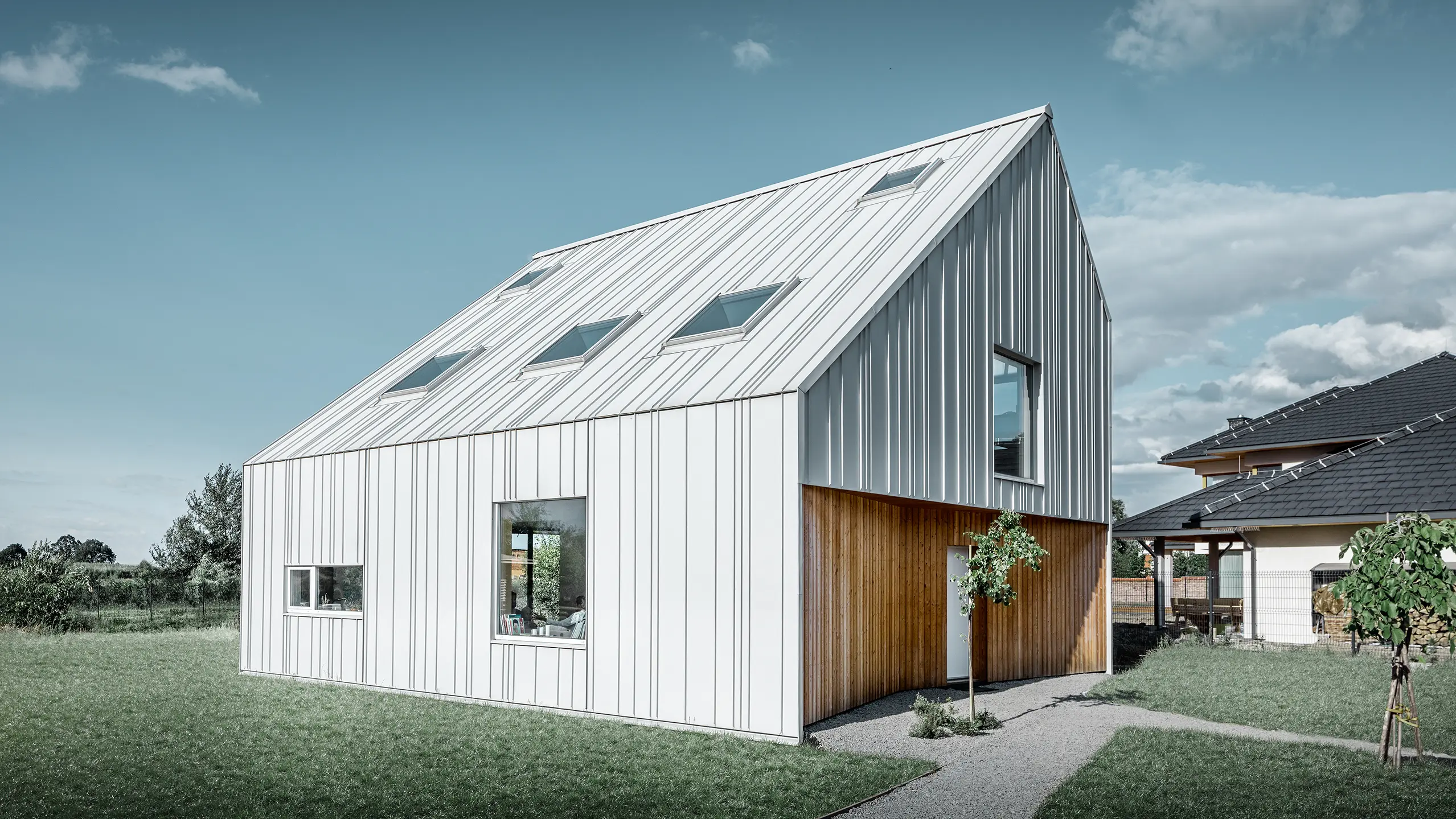 Casa unifamiliare dal taglio moderno con tetto a due falde, l’intero rivestimento esterno è realizzato con PREFALZ in bianco Prefa. Le diverse larghezze delle lastre si estendono dal tetto alla facciata. Sul tetto sono installati diversi lucernari.