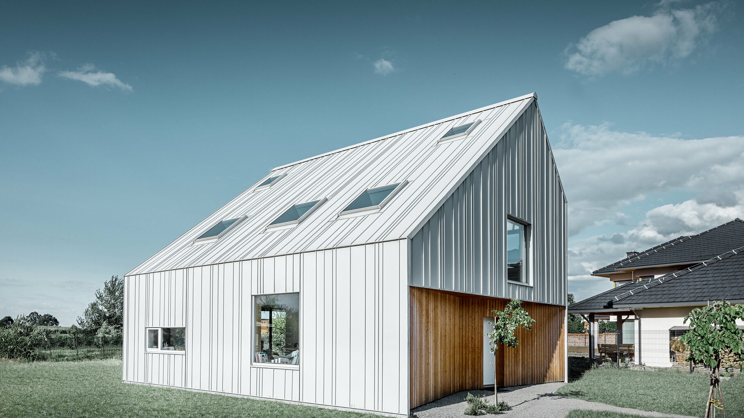 Modern geschnittenes Einfamilienhaus mit Satteldach, die komplette Außenhaut ist mit PREFALZ in Prefaweiß verkleidet. Dabei ziehen sich die unterschiedlich breiten Scharen vom Dach weiter über die Fassade. Im Dach sind mehrere Dachfenster verbaut.