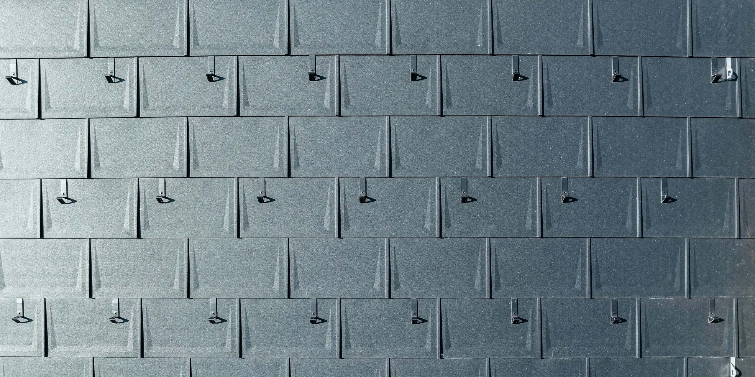 Nahaufnahme einer PREFA Dacheindeckung aus Aluminium. PREFA Dachplatten R.16 in der begehrten Farbe P.10 Anthrazit sind präzise miteinander verbunden. Die hochwertigen Aluminiumplatten bieten eine langlebige, witterungsbeständige und optisch ansprechende Dachlösung. Schneestopper sorgen für zusätzliche Sicherheit.