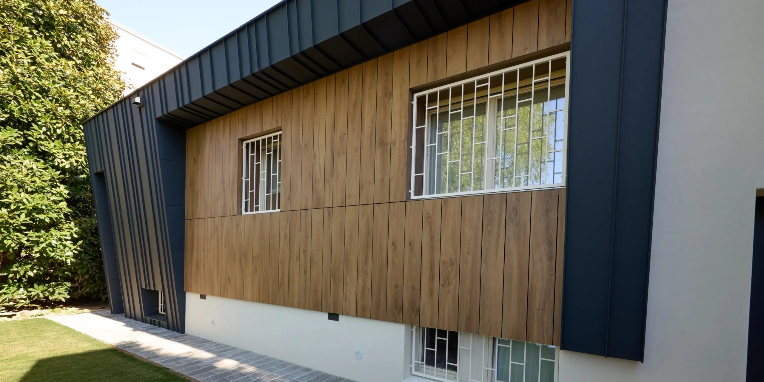 Detailansicht der Villa Castellanza mit markanter PREFALZ Fassade in P.10 Anthrazit und warmen Holzoberflächen. Die präzisen Stehfalzlinien rahmen die Fenster elegant ein und verleihen der Gebäudehülle eine moderne, plastische Wirkung. PREFA Aluminium überzeugt durch Langlebigkeit, Wetterbeständigkeit und hochwertige Architektur, die Design und Funktion harmonisch vereint.