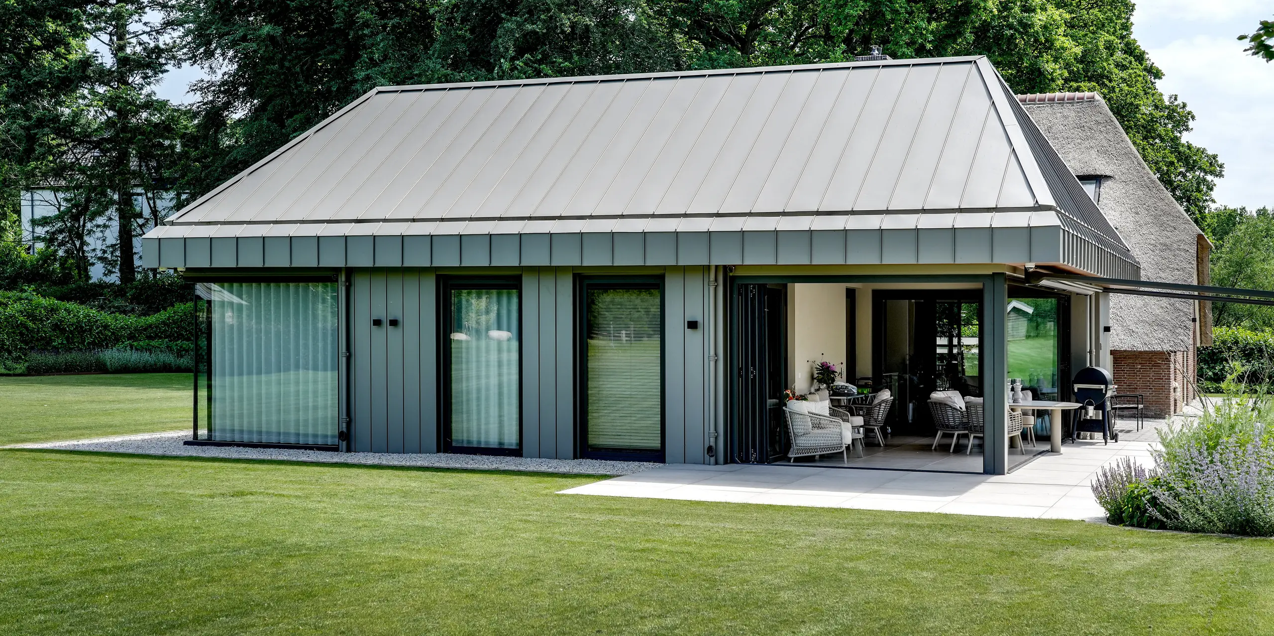 Der moderne Anbau in Putten begeistert mit einer durchgängigen PREFALZ Aluminiumhülle, die Dach und Fassade elegant vereint. Großzügige Glasfronten, die offene Terrassenzone und die präzisen Stehfalze schaffen spannende Blickachsen in die grüne Gartenlandschaft. PREFA Aluminium überzeugt mit langlebiger Qualität, hoher Witterungsbeständigkeit und einer zeitlos modernen Architektur.