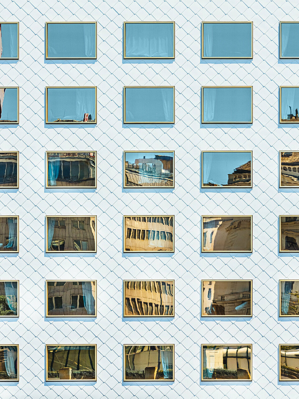 Die Fassade des Hotels THE ROCK Radisson RED Vienna, entworfen von INNOCAD architecture, aus der Normalperspektive; zu sehen sind etliche reinweiße Wandrauten und spiegelverglaste Fenster, welche die Umgebung in sich aufnehmen.