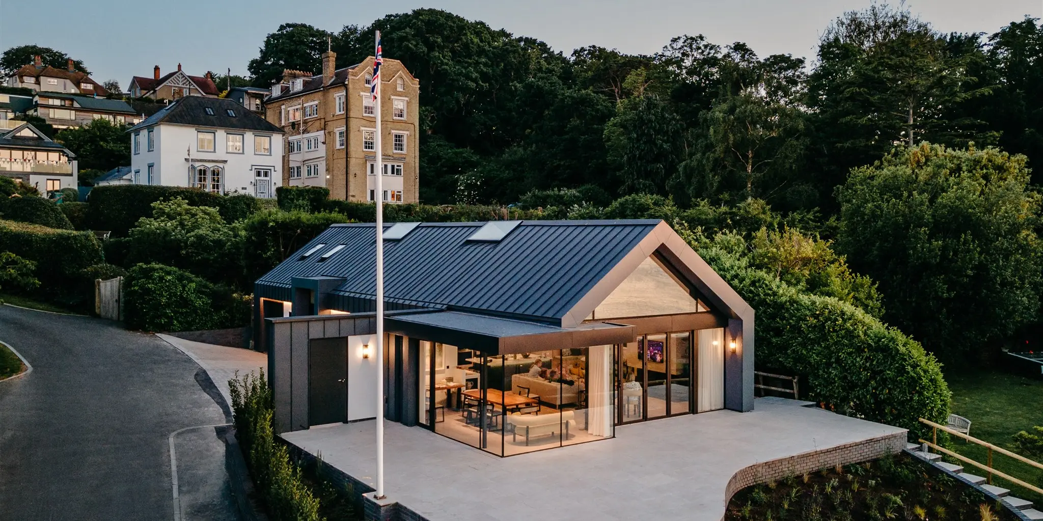 Dieser luxuriöse Bungalow auf der Isle of Wight kombiniert moderne Architektur mit atemberaubender Aussicht. Die dunkelgraue PREFALZ-Gebäudehülle verleiht dem Anwesen eine schlichte Eleganz und integriert es sanft in die üppige Landschaft. Durchdachte Verglasungen maximieren die malerischen Meerblicke und bewahren zugleich die Intimität. Das Haus ist ein perfektes Beispiel für zeitgenössisches Design, das die Schönheit seiner natürlichen Umgebung respektiert und hervorhebt.