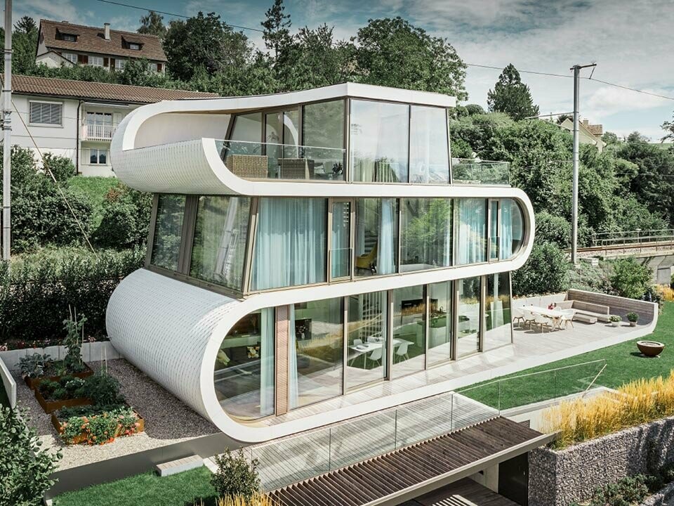 Il Flexhouse al Zürichsee da nell'occhio soprattutto per la sua architettura insolita. I piani sono collegati fra di loro da una parte tramite un arco. La facciata arrotondata é stata rivestita con la Scaglia piccola di PREFA nel colore bianco puro, che si adatta idealmente agli archi.