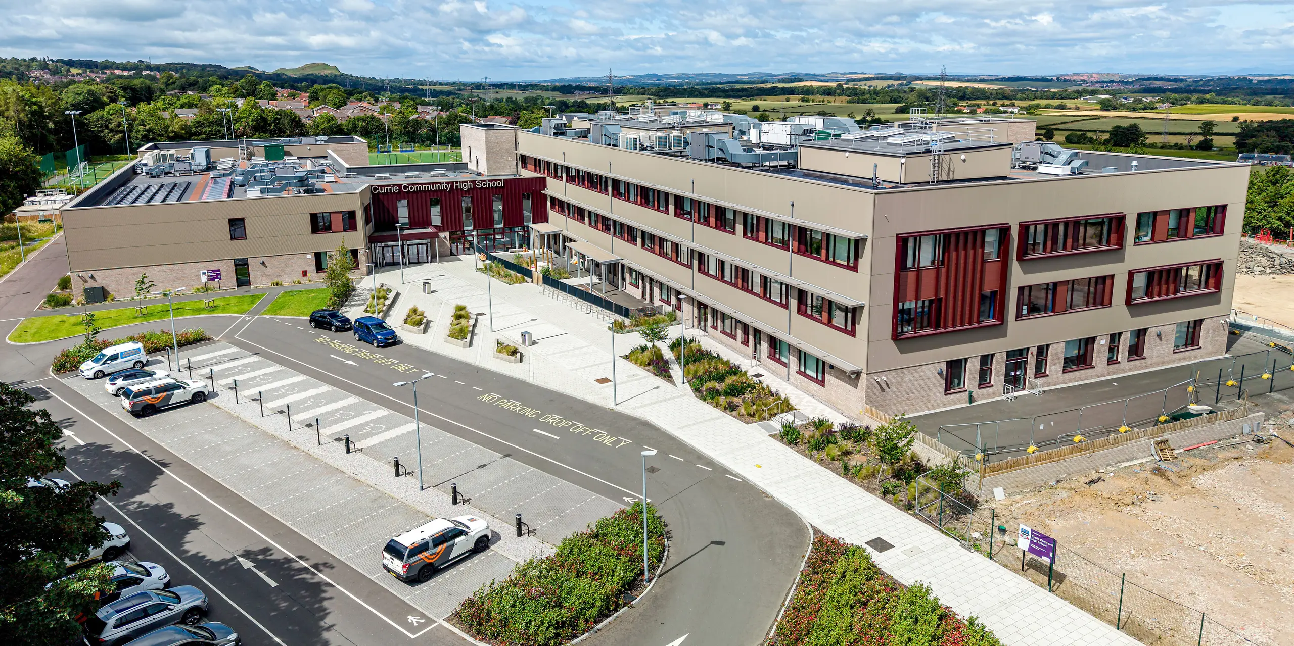 Die Luftaufnahme der Currie Community High School in Edinburgh setzt die moderne PREFA Fassade eindrucksvoll in Szene. Das Strangpressprofil Zacke in P.10 Prefabronze verleiht den weitläufigen Gebäudekörpern eine markante Struktur und elegante Tiefenwirkung. Die vertikalen Fassadenlinien setzen spannende Akzente im Tageslicht, während das langlebige, korrosionsbeständige Aluminium mit Wartungsarmut und zeitloser Architekturqualität überzeugt.