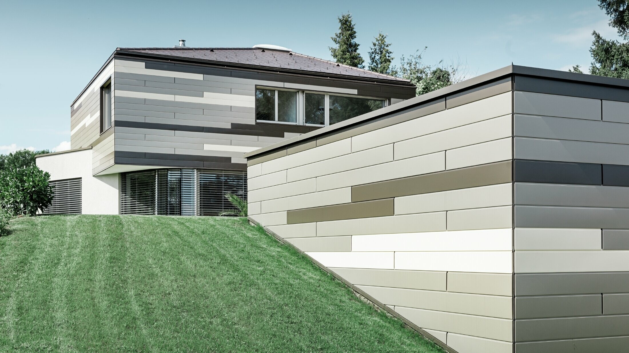Casa unifamiliare moderna con copertura piana e terrazzo coperto con un'allestimento facciata personalizzato in alluminio in doghe in marrone, bronzo e avorio di PREFA