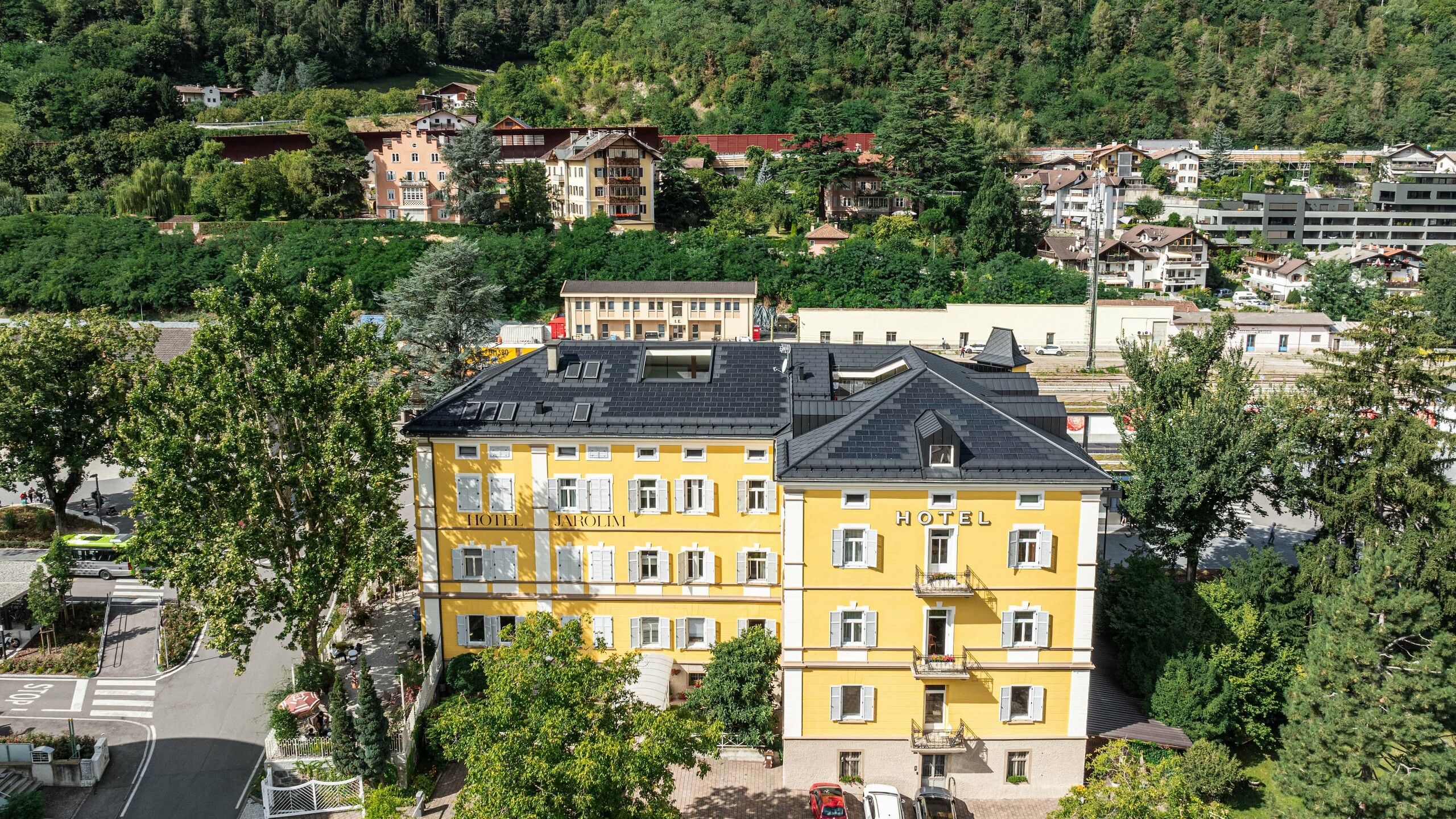 Vista dall'alto dello storico Hotel Jarolim ristrutturato in tegole fotovoltaiche PREFA, con davanti il giardino e sul retro la stazione ferroviaria di Bressanone.