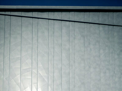 Zwei ArchitektInnen begutachten die PREFA Siding.X Fassade die in durch die Sonneneinstrahlung in verschiedenen Spiegelungen erscheint