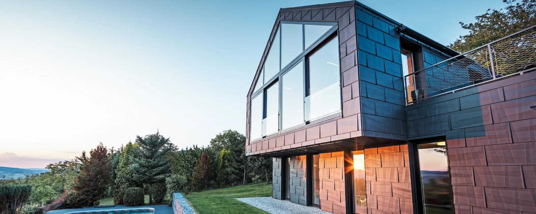 Aluminiumfassade eines Einfamilienhauses mit PREFA Fassadenpaneelen FX.12 in P.10 Anthrazit bei Sonnenuntergang. 