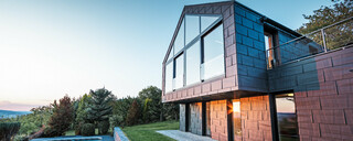 Aluminiumfassade eines Einfamilienhauses mit PREFA Fassadenpaneelen FX.12 in P.10 Anthrazit bei Sonnenuntergang. 