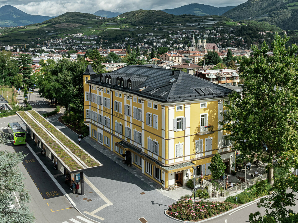 Panoramablick auf das Hotel Jarolim in Brixen, ausgestattet mit einem modernen PREFA Dach aus Solardachplatten und Dachplatten R.16. Das langlebige und witterungsbeständige Aluminiumdach verbindet nachhaltige Energiegewinnung mit eleganter Ästhetik und fügt sich harmonisch in die denkmalgeschützte Architektur des Gebäudes ein. Umgeben von der malerischen Südtiroler Landschaft zeigt das Hotel, wie sich Tradition und Innovation perfekt verbinden lassen.