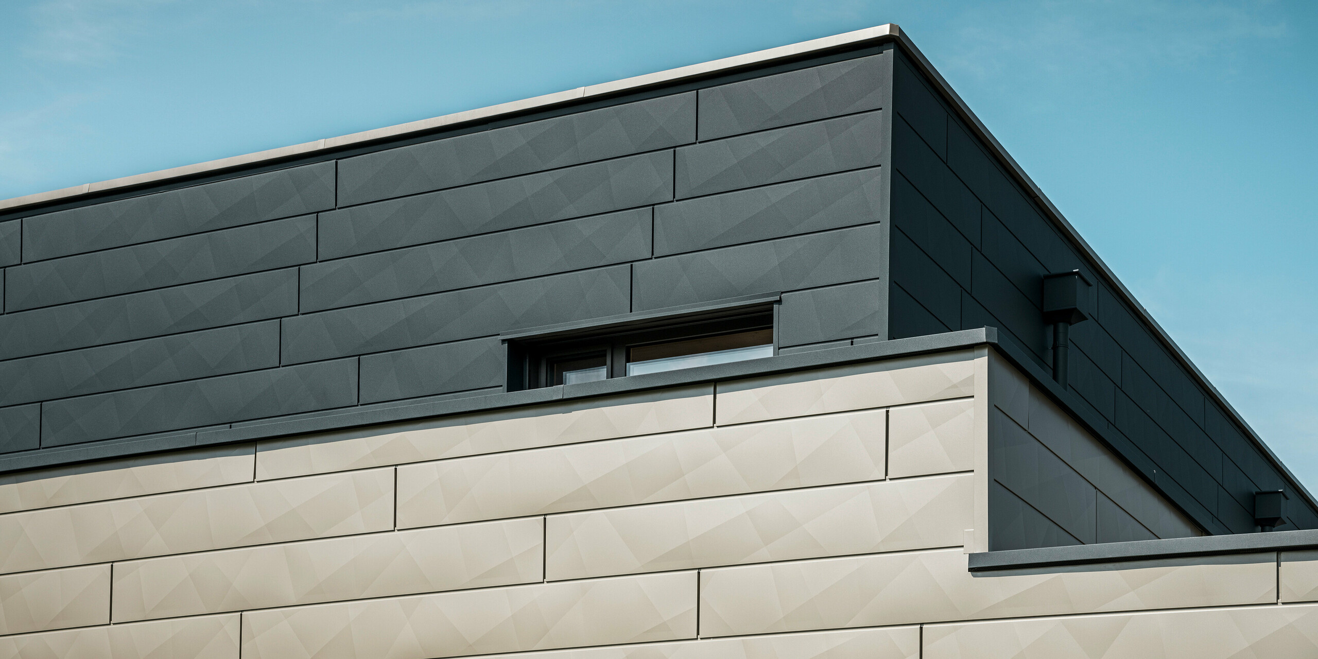 [Translate to Italiano:] Nahaufnahme der zweifarbigen PREFA Aluminiumfassade eines modernen Einfamilienhauses in Wippenham, Österreich. Die Fassade ist mit Siding.X Fassadenpaneelen in den Farben Anthrazit und Bronze gestaltet, die ein elegantes und dynamisches Erscheinungsbild erzeugen. Die präzise Verarbeitung und das Zusammenspiel der Farben betonen die zeitgemäße Architektur des Gebäudes.