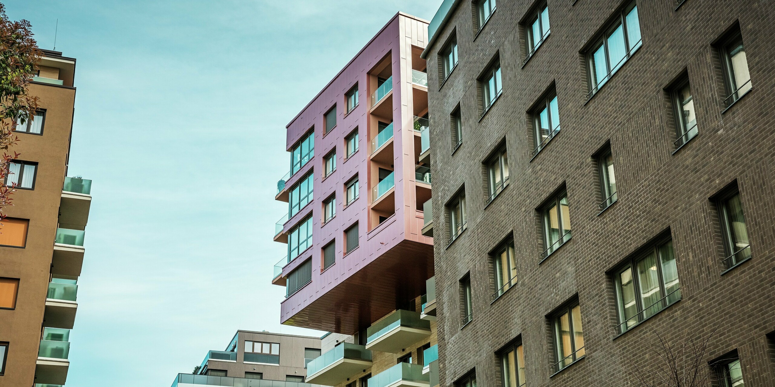 Blick auf das prägnante, auskragende Gebäudeelement des Grand Corvin Projekts im Budapester Corvin-Viertel. Die oberen Etagen sind mit PREFA Siding Fassadenpaneelen in vertikaler Verlegung und der Sonderfarbe Lachsmetallic verkleidet. Die langlebige Aluminiumfassade hebt sich deutlich von der umgebenden Ziegelarchitektur ab und unterstreicht den modernen, architektonischen Charakter des revitalisierten Stadtteils.