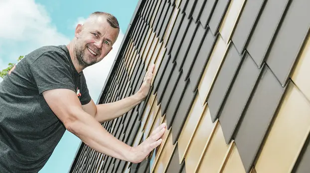 PREFA Handwerker mit grauem T-Shirt an einer PREFA Rauten-Fassade in Braun und Mayagold.