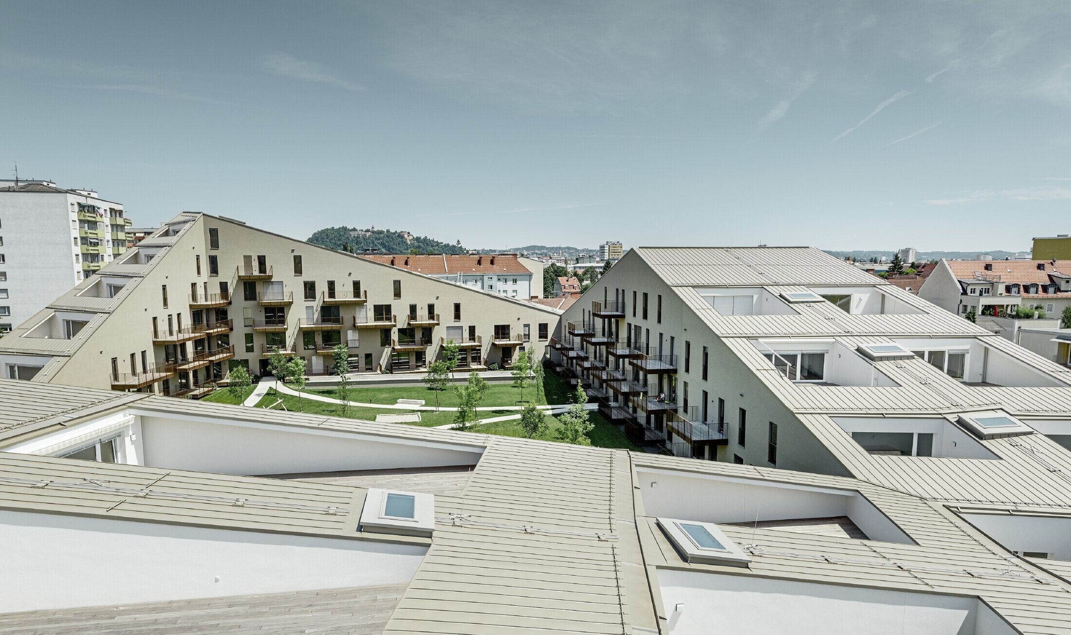 lang gezogene Wohnhausanlage in Graz mit flachen Dachflächen und integrierten Terrassen und großflächigen Fenstern mit einem Prefalzdach in der Sonderfarbe broncemetallic