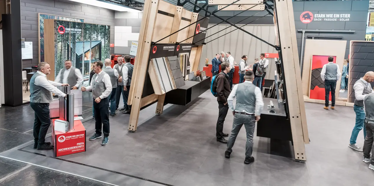 Affollato stand PREFA con pareti espositive dedicate ai prodotti PREFA in alluminio per tetti e facciate.