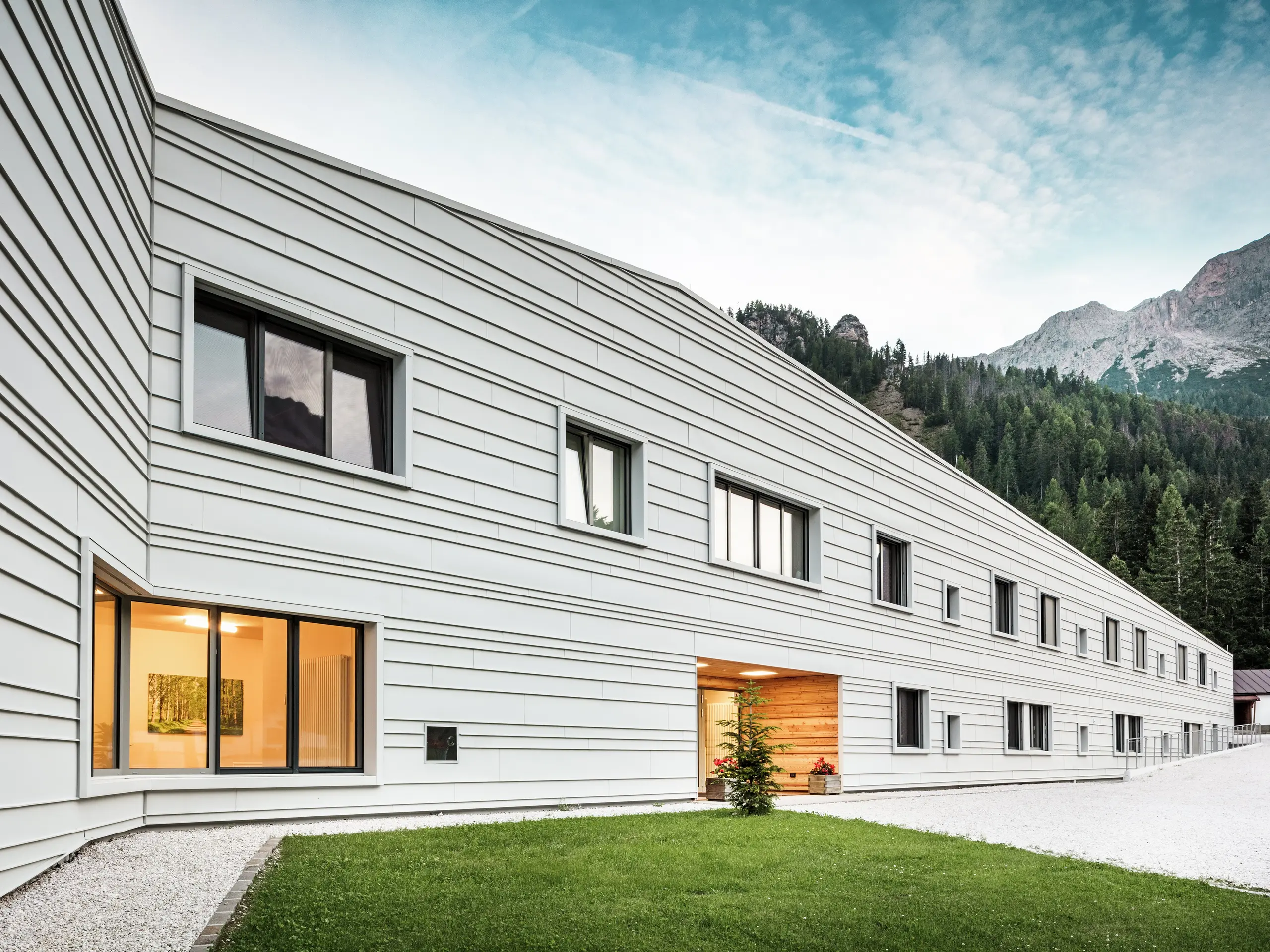 La moderna caserma “Tempesti” in Alto Adige colpisce per il design chiaro della facciata in PREFALZ P.10 nel colore bianco PREFA. Le lastre di alluminio posate in modo orizzontale e a intervalli irregolari conferiscono all'edificio un aspetto visivamente più lungo. La facciata in alluminio chiaro riflette la luce solare e garantisce così un microclima migliore. La moderna caserma è una dichiarazione architettonica nel cuore della natura alpina.