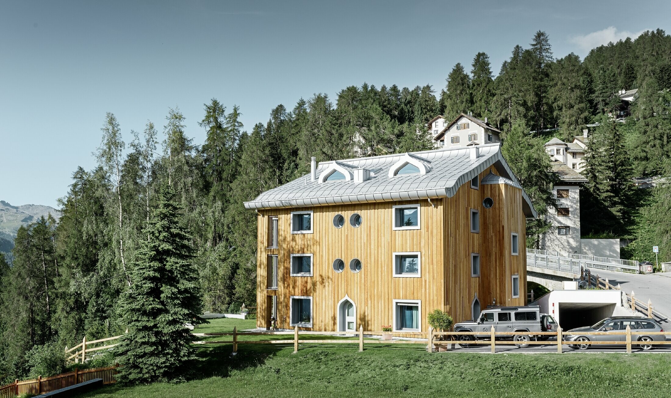 Complesso residenziale a St. Moritz con facciata in legno e copertura in alluminio con grondaia curva in silver metallizzato