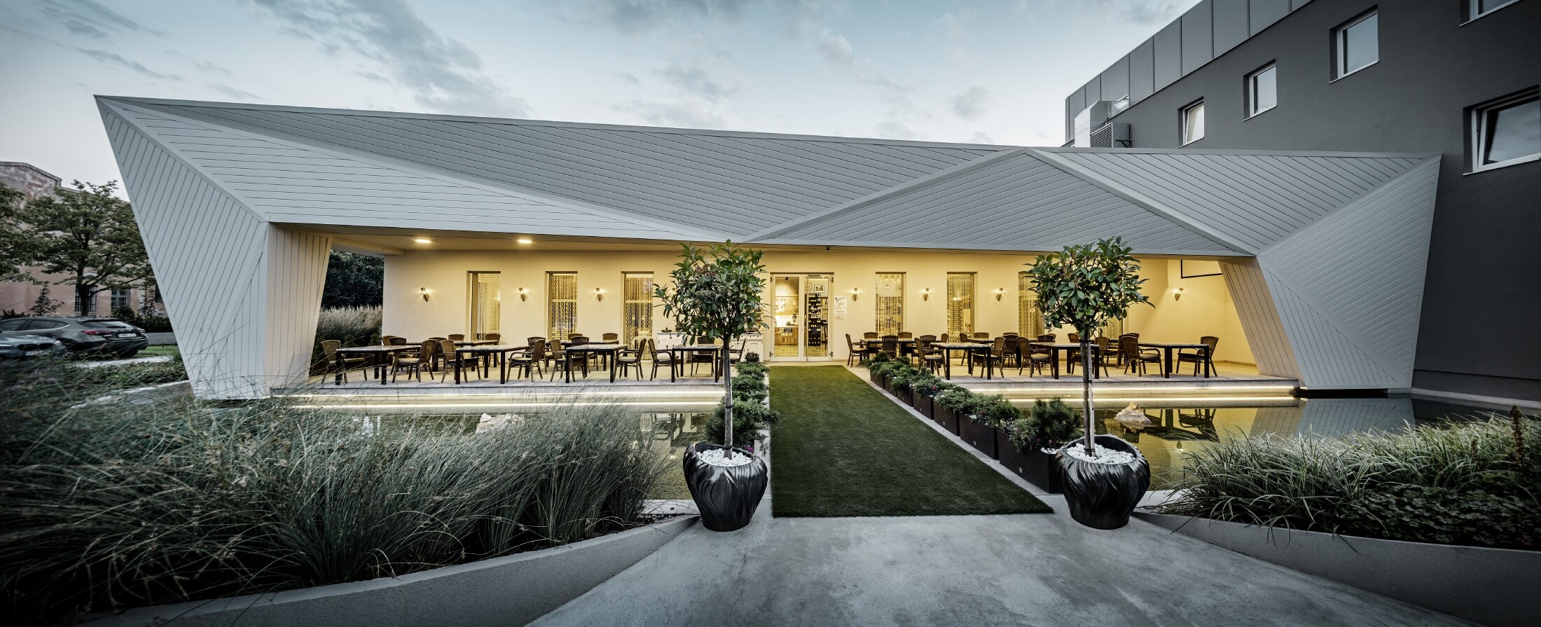 Giardino per gli ospiti del ristorante Mimama a Budapest, Ungheria. La facciata del ristorante è rivestita con le doghe di rivestimento PREFA in bianco prefa.