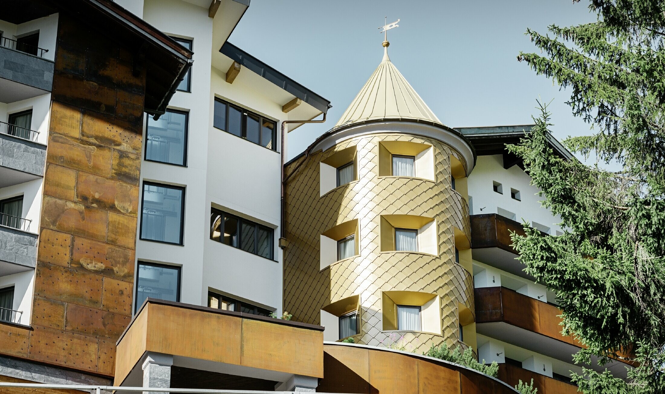 traditionelles Hotel in Ischgl mit Holzbalkonen und Holzfassade und einem Turm mit goldenen Alu-Rauten von PREFA