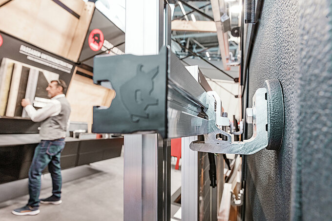 PRE-VARIO sustav za montažu solarnih panela tvrtke PREFA u detalju: Robusna aluminijska potpornja omogućuje stabilnu montažu na različitim krovnim konstrukcijama. Dugotrajna, otporna na koroziju i idealna za učinkovitu i vremenski štedljivu montažu fotonaponskih sustava. Pogled s boka otkriva zanimivu perspektivu stabilnog PV sustava za montažu. U pozadini se vidi PREFA zaposlenik. Snimka je nastala u sklopu sajma BAU München 2025, gdje je inovativni proizvod predstavljen po prvi put.