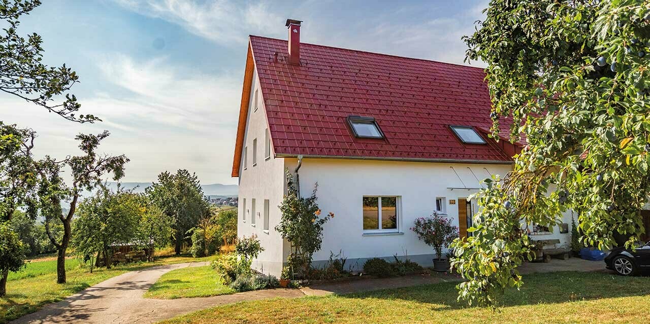 Romantisches Häuschen am land mit viel Bäumen und Sträuchern. Eingedeckt mit einem PREFA Dach in Oxydrot.