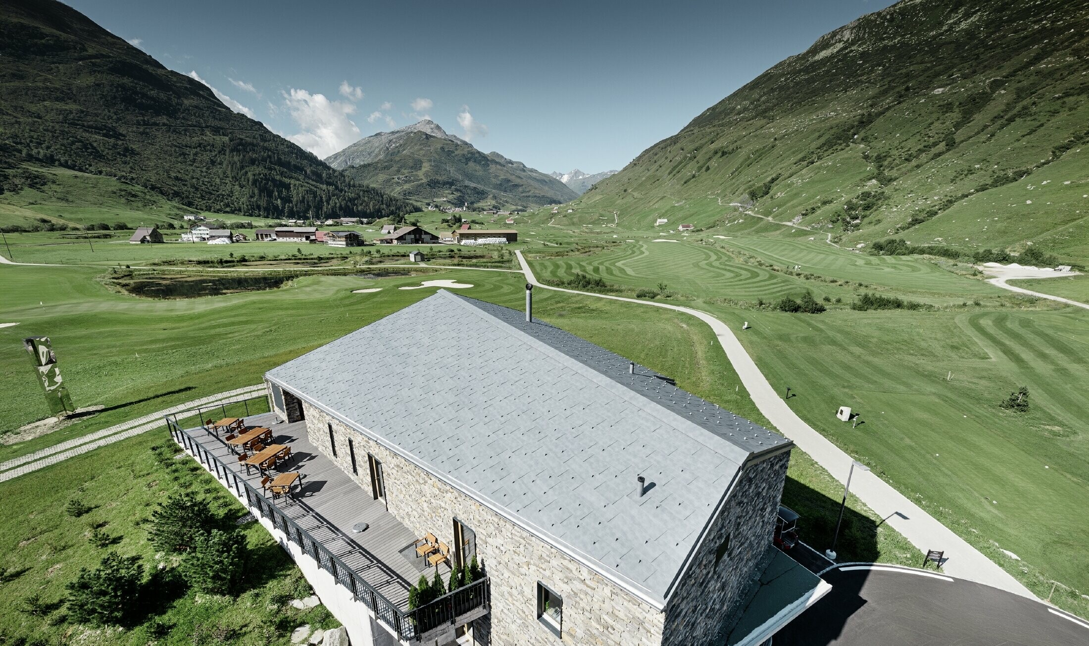 Il moderno punto di ritrovo del campo da golf a Andermatt con una facciata in pietra e il pannello per coperture FX.12 PREFA in alluminio in grigio pietra