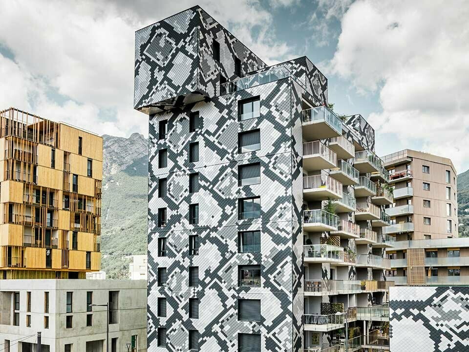 condominio moderno e nuovo a Grenoble, rivestito con scaglia in alluminio, la fantasia ricorda la pelle di un pitone in antracite, grigio chairo, alluminio naturale e silver metallizzato, accanto un condominio color sabbia sotto un cielo nuvoloso