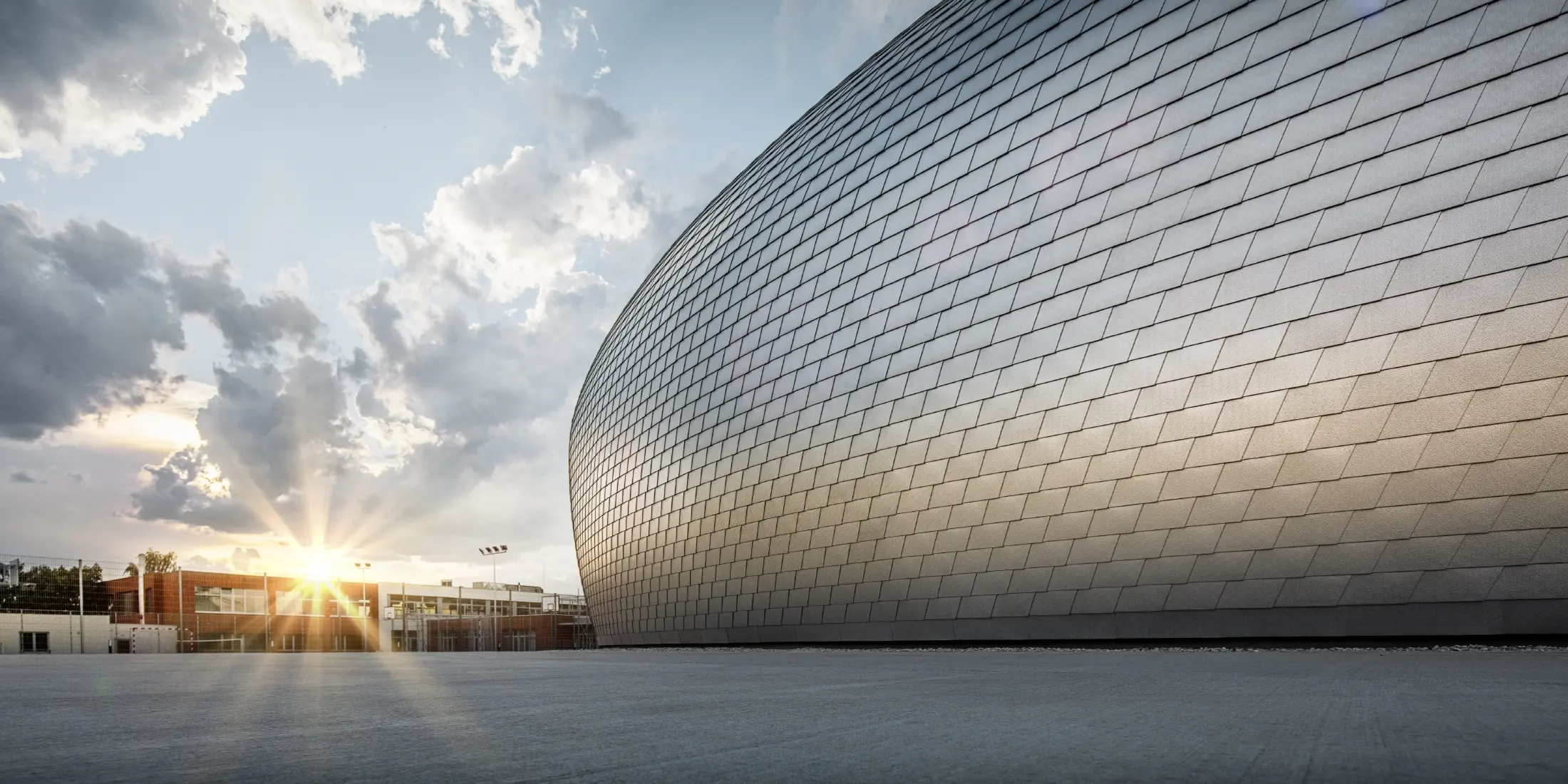 Sporthalle in Tschechien in Form eines UFOs verkleidet mit der PREFA Wandschindel in Naturblank bei Sonnenaufgang.