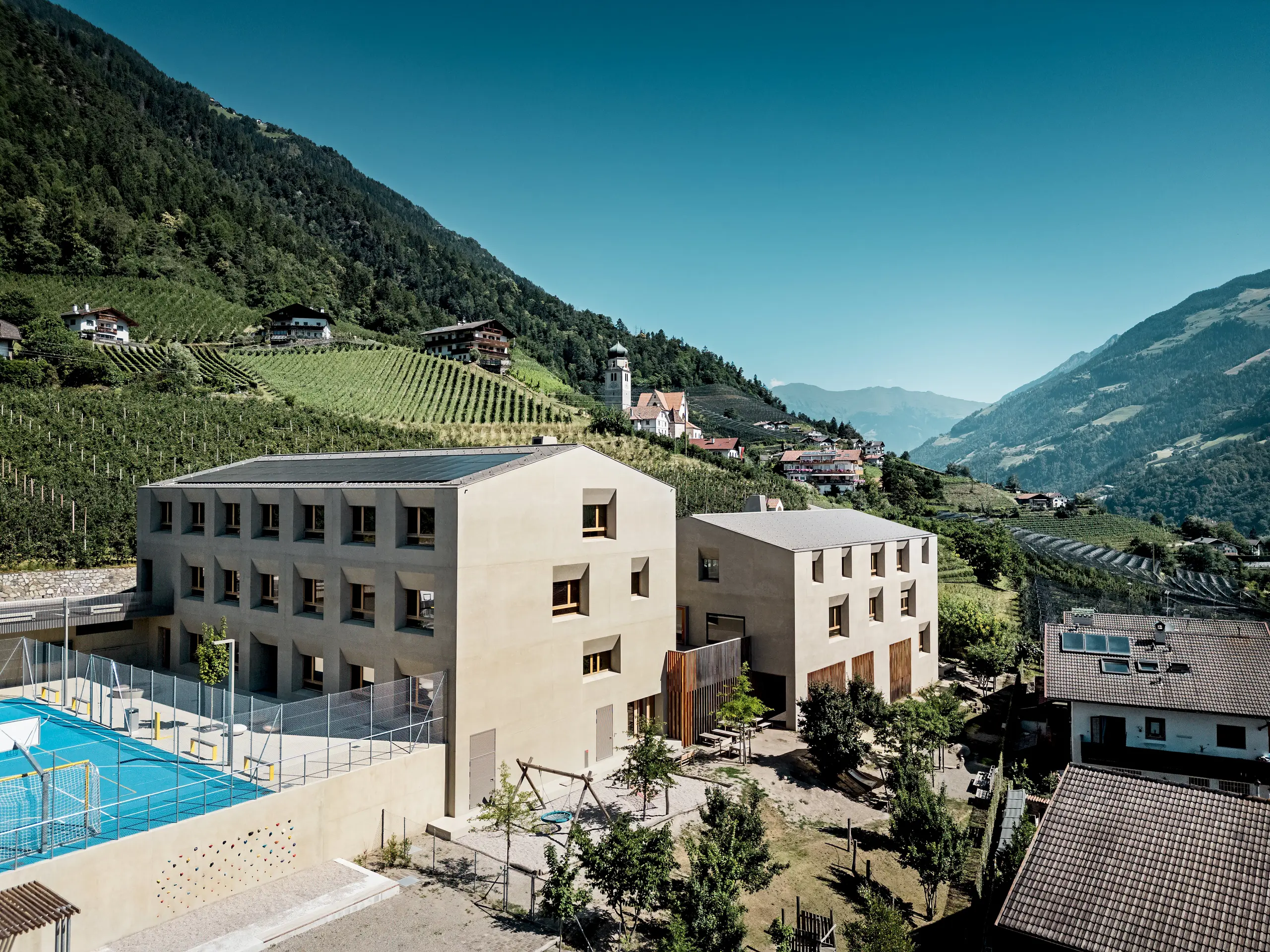Il centro educativo di Riffian, in Alto Adige, presenta la scuola materna e la scuola elementare come un armonioso complesso architettonico immerso nel paesaggio montano. Le scaglie 44 × 44 PREFA nella finitura P.10 bronze conferiscono agli edifici un aspetto elegante, offrono una protezione duratura dagli agenti atmosferici e si integrano perfettamente nell’ambiente naturale.