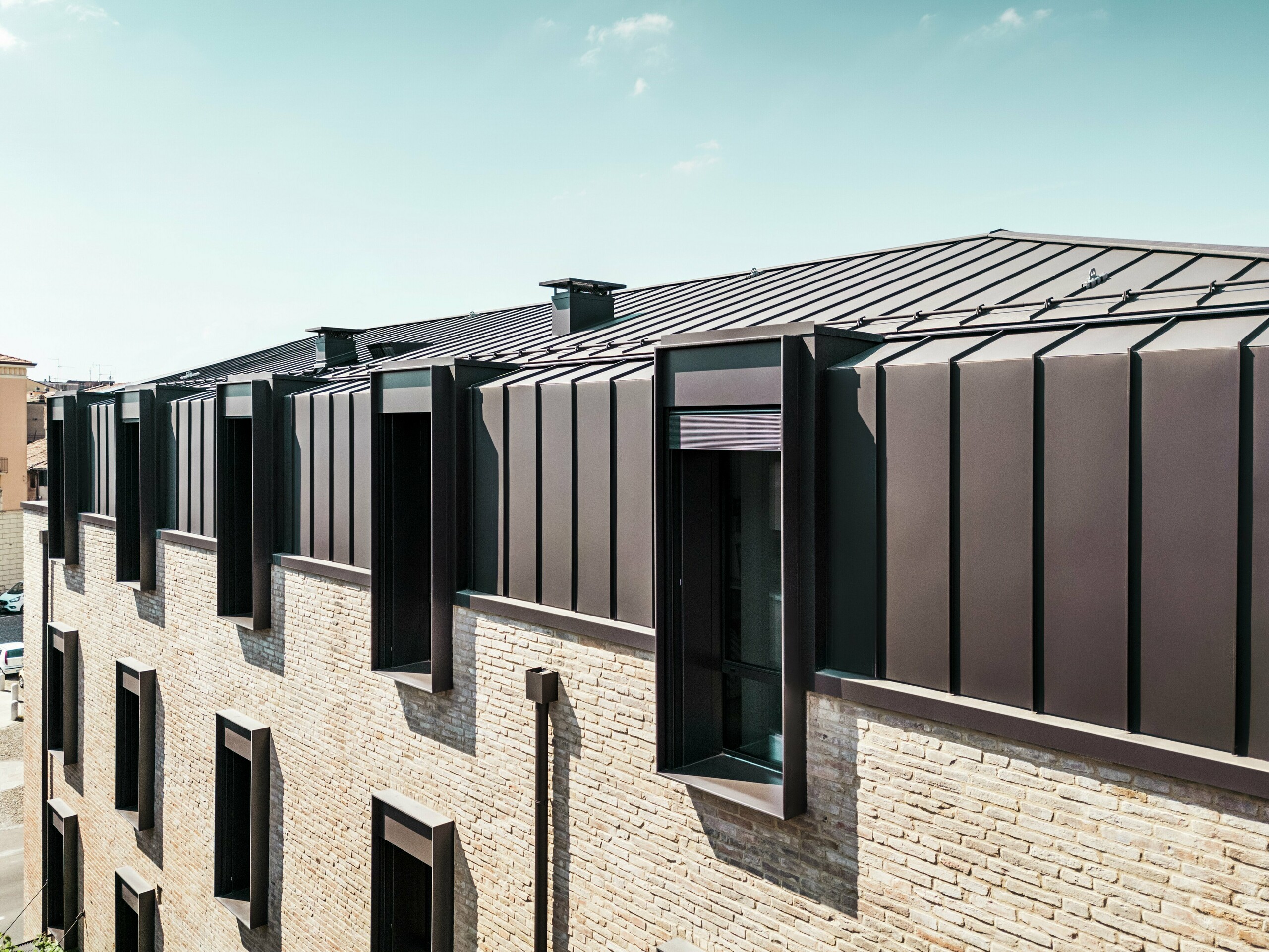 Moderne Dach- und Fassadengestaltung eines Backsteinhauses in Italien mit PREFALZ Aluminiumdach in der Farbe P.10 Nussbraun und markanten Fenstergauben