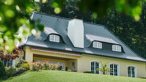 Casa monofamiliare con nuovo tetto ristrutturato con scandole PREFA color antracite con abbaini arrotondati (abbaini a pipistrello) e camino bianco.