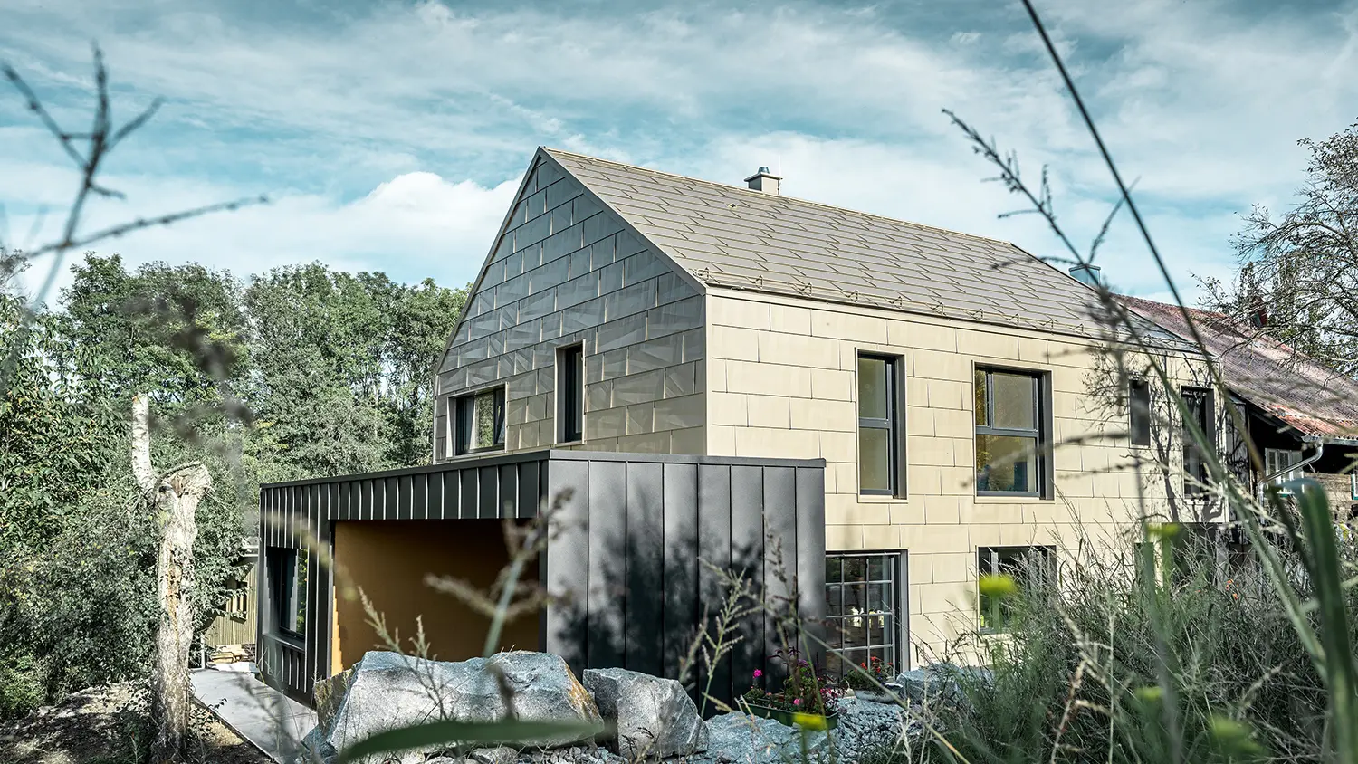 L'edificio residenziale senza grondaie è rivestito sul tetto e sulla facciata con il pannello FX.12 in alluminio PREFA nel colore bronzo. Proprio accanto è visibile un garage con tetto piatto e facciata con aggraffatura angolare.