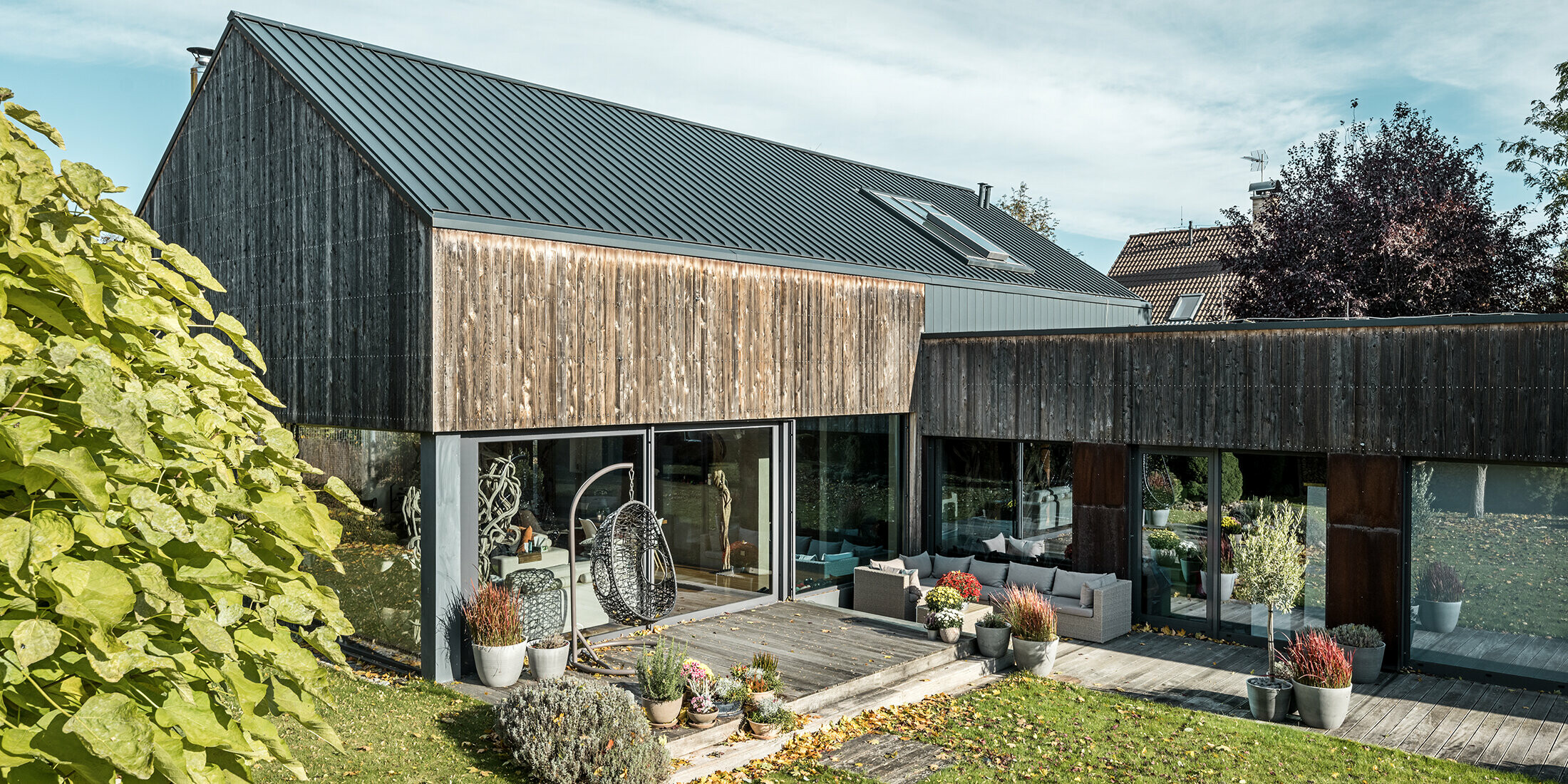 Casa unifamiliare con tetto a due falde, rivestito con aggraffatura doppia PREFALZ in antracite e facciata di legno invecchiata. Con una bella terrazza in legno e grandi finestre al piano terra.