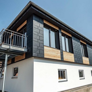La parte superiore dell'edificio è stata rivestita con una combinazione di pannelli orizzontali in legno di larice e di pannelli in alluminio Doga.X PREFA di colore antracite.