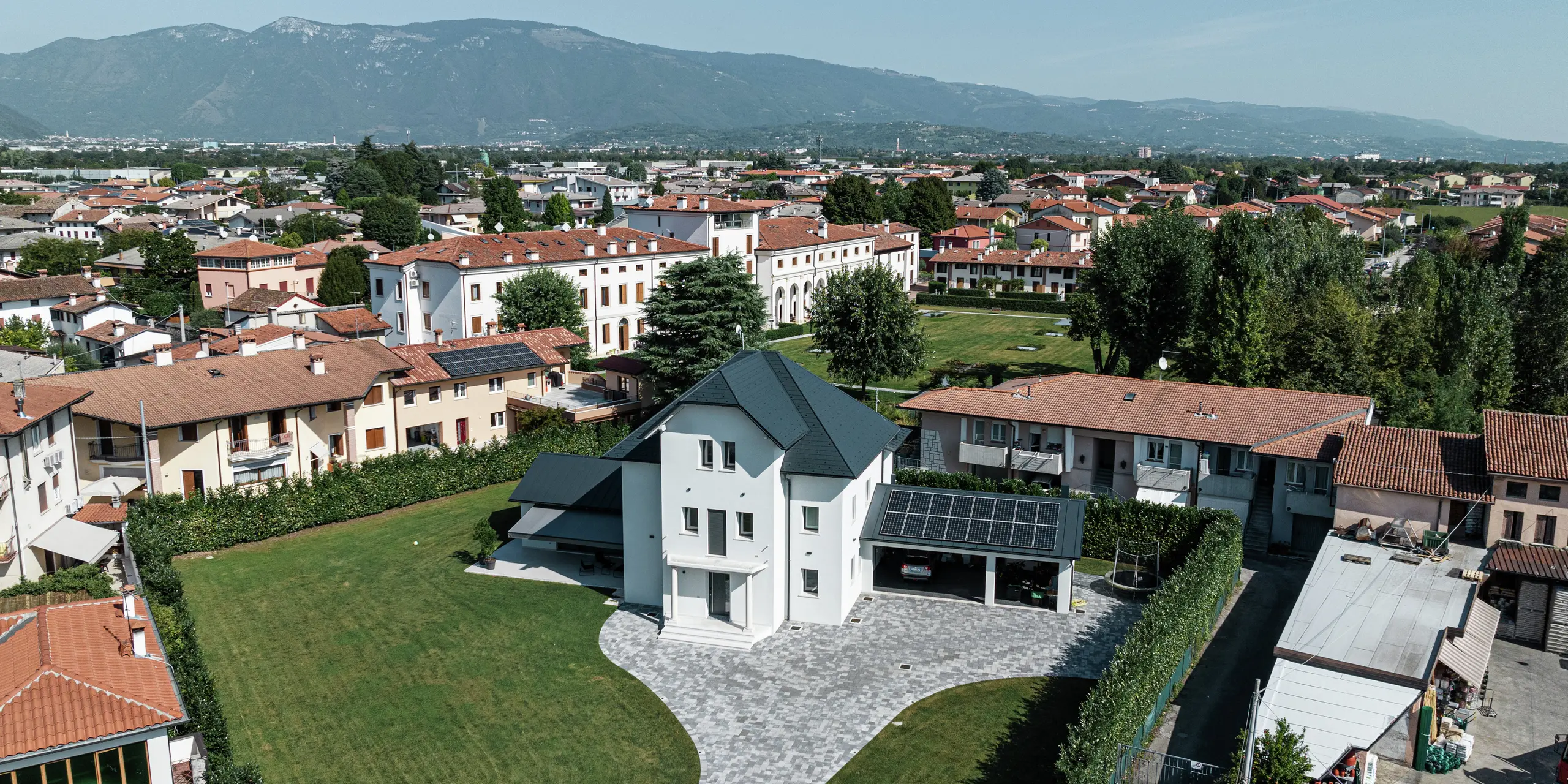 Luftaufnahme eines modernen Einfamilienhauses in Marano Vicentino, Italien, mit einem robusten Dach aus PREFA Dachschindeln in P.10 Anthrazit. Die angrenzenden Nebengebäude sind mit einer klassischen Doppelstehfalzdeckung aus Aluminium versehen. Die hochwertige Aluminiumeindeckung sorgt für eine langlebige und ästhetische Dachgestaltung.