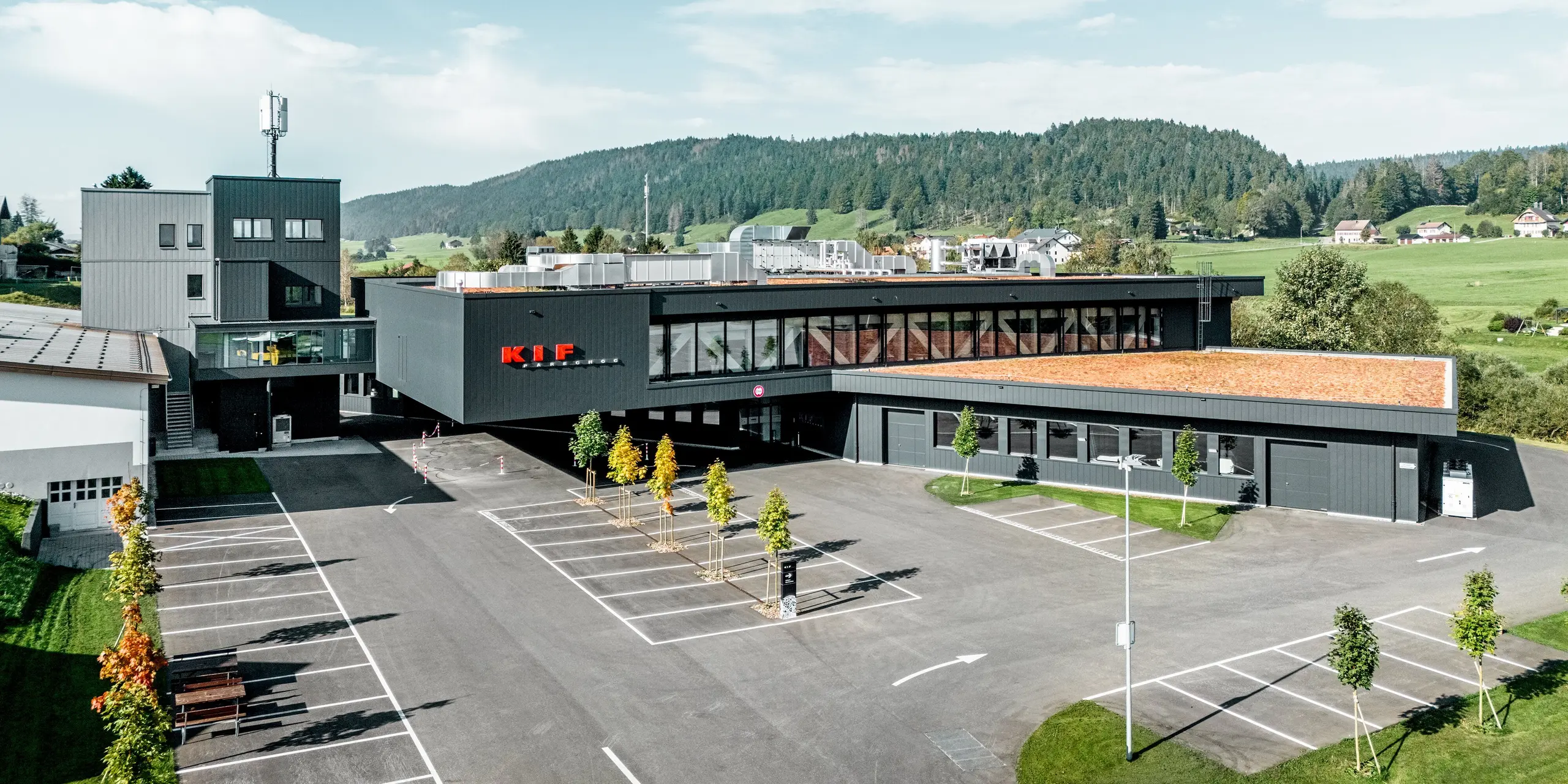 Luftaufnahme des Firmengebäudes von KIF Parechoc in Le Brassus: Die weitläufige Anlage fügt sich harmonisch in die grüne Hügellandschaft ein. Die Fassade mit PREFA Sidings in P.10 Anthrazit und Patinagrau betont die klare, moderne Architektur und die markanten Gebäudekanten. Das langlebige Aluminium überzeugt durch hohe Witterungsbeständigkeit, Korrosionsschutz und geringen Wartungsaufwand bei dauerhaft hochwertiger Optik.